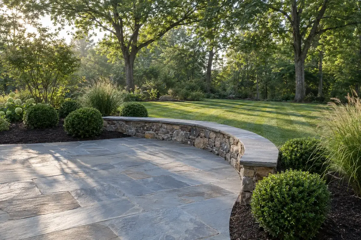 After: the same yard with a stone patio, seat wall, planted beds and a green lawn
