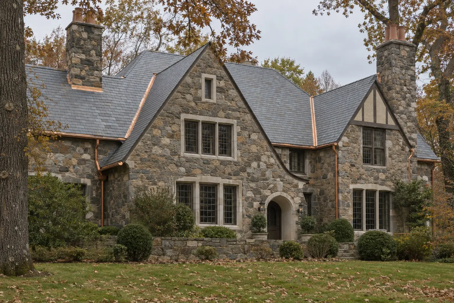 A fieldstone Tudor house with a natural slate roof and copper gutters among autumn oaks